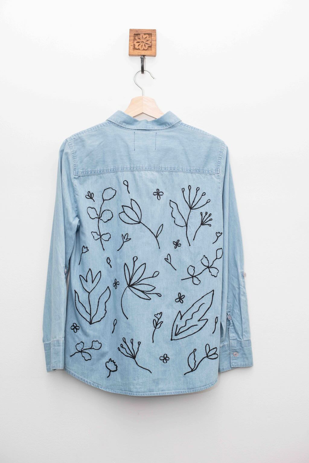 Back of light denim shirt is covered with black outline embroidered botanical forms. 